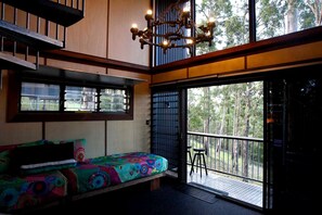 Une chambre avec un lit aux couleurs vives, un balcon doté d’une rambarde et une vue sur les arbres.