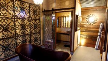 A bathroom with a freestanding bathtub, a shower with a glass door, and a wooden wall with a decorative light fixture.