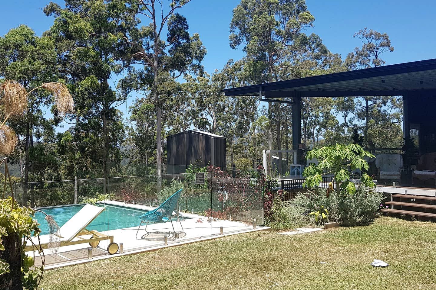 A backyard with a swimming pool, a covered patio, and a fenced area with trees.