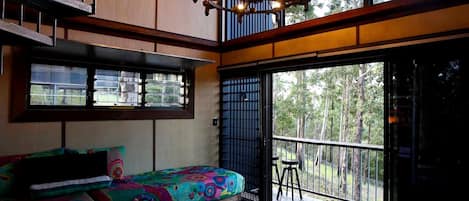 A room with a colorful bed, a balcony with a railing, and a view of trees.
