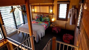 A cozy cabin-style bedroom with a bed, colorful pillows, a hanging light fixture, and a window with clothes hanging outside.