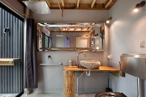 A compact bathroom with a wooden vanity, a stone sink, and a mirrored wall.