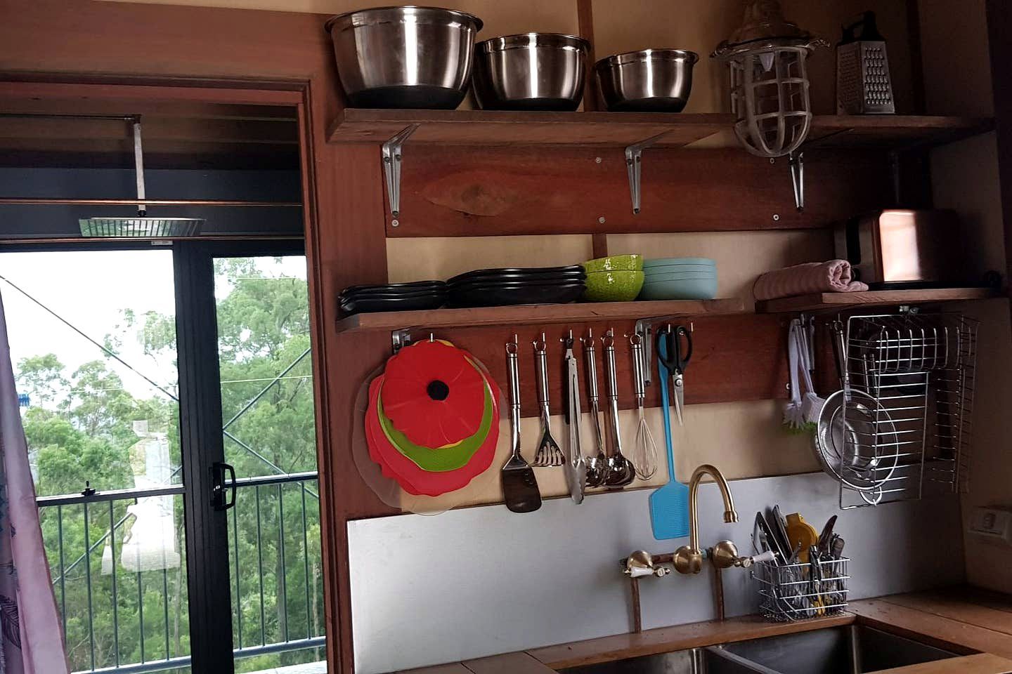A kitchen with shelves holding various utensils, a hanging pot rack, and a window with a view of greenery.