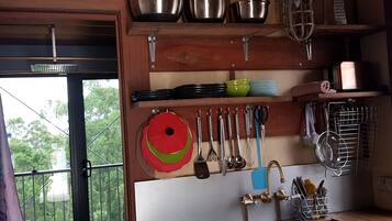 A kitchen with shelves holding various utensils, a hanging pot rack, and a window with a view of greenery.