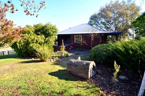 A house with a covered porch, surrounded by a well-maintained garden with various plants and a large log.
