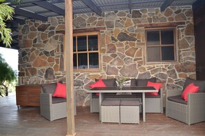 A stone-walled outdoor seating area with wicker furniture and red cushions.
