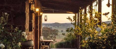 A wooden deck leading to a covered outdoor area with rustic stone walls, potted plants, and a view of the countryside.
