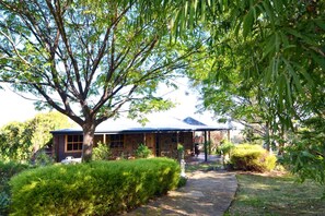 A stone house with a covered porch, surrounded by lush greenery and a stone pathway.