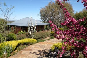 A house with a stone pathway leading to a covered porch, surrounded by well-maintained gardens and flowering plants.
