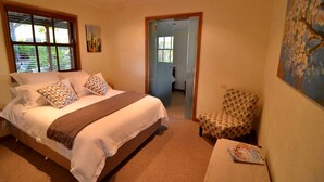 Een slaapkamer met een bed, een stoel, een schilderij en een deur naar een andere kamer.