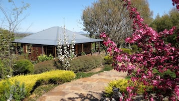 A house with a stone pathway leading to a covered porch, surrounded by well-maintained gardens and flowering plants.
