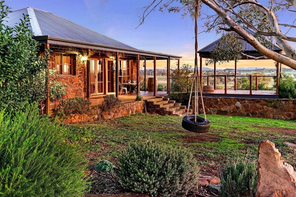 A stone house with a porch, a swing, and a view of the countryside.