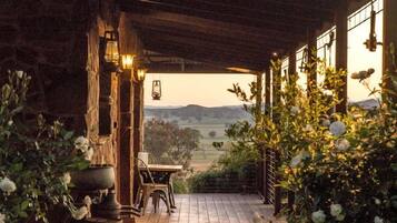 Une terrasse en bois mène à un espace extérieur abrité, agrémenté de murs en pierre rustique, de plantes en pot et offrant une vue sur la campagne.