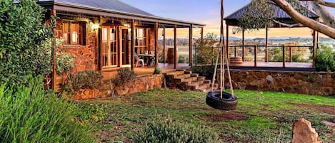 A stone house with a porch, a swing, and a view of the countryside.