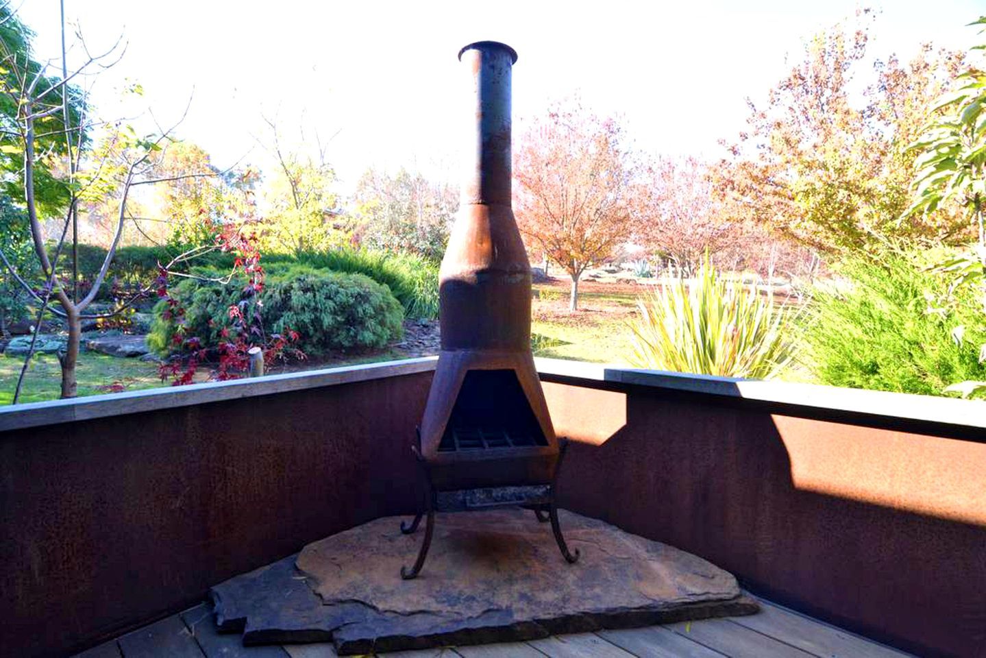 A wood-burning stove on a patio with a view of a garden.