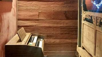 A room with wooden walls, a piano, a small stool, and a window with a view.