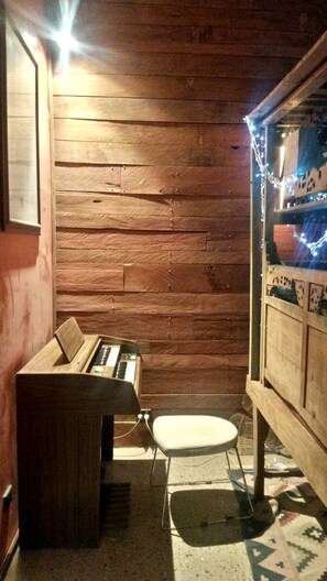 Una habitación con paredes de madera, un piano, un pequeño taburete y una ventana con vistas.