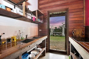 A rustic kitchen with wooden shelves, a sink, and a view of the outdoors.