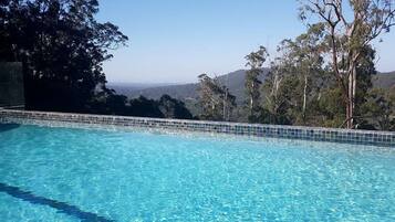 Ein klares, blaues Schwimmbecken mit Fliesenrand, umgeben von Bäumen und Blick auf ferne Hügel.