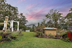 A garden with a pergola, a small pool, and a white fence.