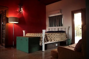 A room with a bed, a floor lamp, a radiator, and a window with curtains.