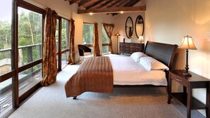 A bedroom with a large bed, a desk, two chairs, a dresser, and a window with curtains.