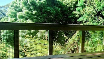 Una taza de café blanco sobre una mesa de madera, con vistas a árboles verdes a través de una valla de malla.