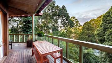 A wooden deck with a table and chairs, surrounded by a mesh fence and trees.