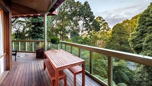 A wooden deck with a table and chairs, surrounded by a mesh fence and trees.
