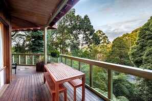 A wooden deck with a table and chairs, surrounded by a mesh fence and trees.