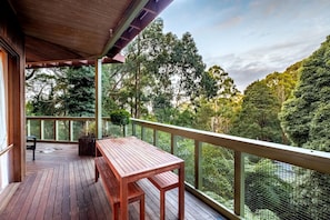 Une terrasse en bois avec une table et des chaises, entourée d’une clôture en treillis et d’arbres.