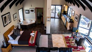 A spacious room with a large bed, a sitting area with a sofa, a kitchen area, and a bathroom with a bathtub.