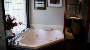 A bathroom with a large bathtub, a window with frosted glass, and a sink.