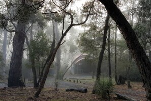 A forested area with a building that appears to be a lodge or cabin, surrounded by trees and a misty atmosphere. - Marvelous Halls Gap Cabin Ideal for Romantic Getaways in Victoria (Halls Gap)