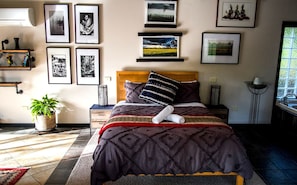 A neatly arranged bedroom with a bed, bedside tables, a potted plant, and framed pictures on the wall.