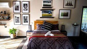 A neatly arranged bedroom with a bed, bedside tables, a potted plant, and framed pictures on the wall.