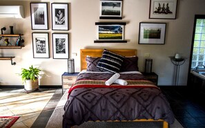 Une chambre à coucher bien rangée, avec un lit, des tables de chevet, une plante en pot et des tableaux encadrés accrochés au mur.
