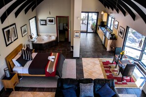 A spacious room with a large bed, a sitting area with a sofa, a kitchen area, and a bathroom with a bathtub. - Marvelous Halls Gap Cabin Ideal for Romantic Getaways in Victoria (Halls Gap)