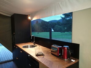 Una cocina compacta con un lavabo, un tostador y una tetera, con un ventanal que ofrece vistas a un paisaje verde.