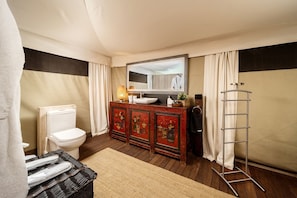 A bathroom with a toilet, a sink, a mirror, a cabinet with decorative panels, a shower curtain, and a towel rack.