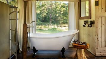 A bathroom with a freestanding bathtub, a wooden vanity, a mirror, and a window with a view of trees.