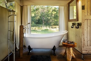 A bathroom with a freestanding bathtub, a wooden vanity, a mirror, and a window with a view of trees.