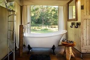 A bathroom with a freestanding bathtub, a wooden vanity, a mirror, and a window with a view of trees. - Kalahari Safari tent in Obi Obi, Queensland (Obi Obi)