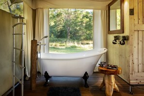 A bathroom with a freestanding bathtub, a wooden vanity, a mirror, and a window with a view of trees.