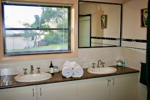 A bathroom with two sinks, a window with blinds, a mirror, and a towel rack.