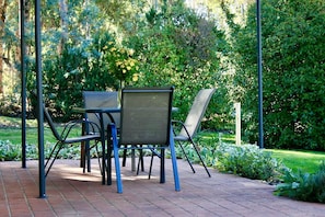 A patio with a table and chairs, surrounded by greenery.