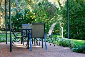 Eine Terrasse mit Tisch und Stühlen, umgeben von viel Grün.