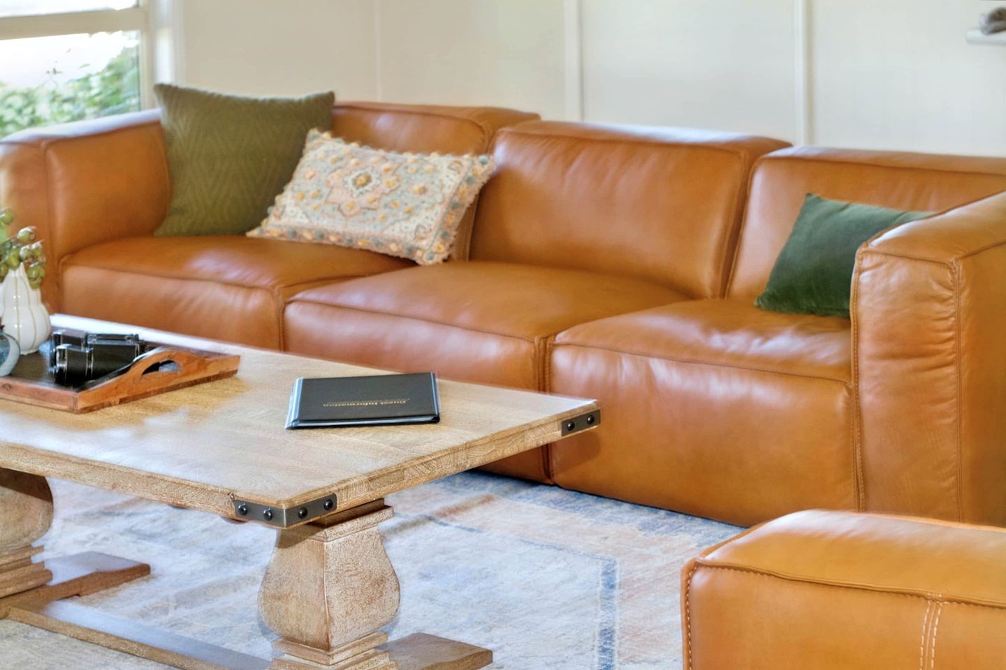 A brown leather sofa with cushions, a wooden coffee table with a book and a decorative item, and a marble floor.
