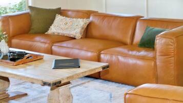 A brown leather sofa with cushions, a wooden coffee table with a book and a decorative item, and a marble floor.