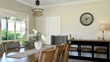 A dining area with a wooden table, chairs, a vase with flowers, a wall clock, and a lamp.